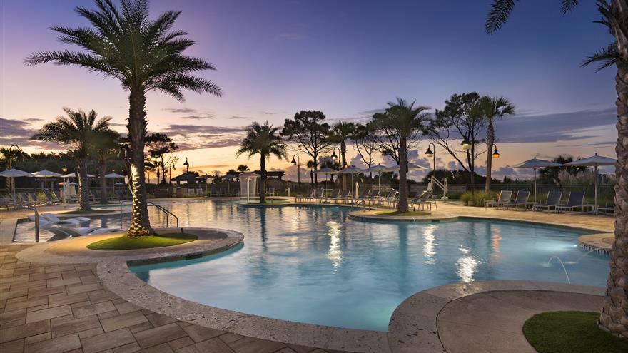 Pool and courtyard surrounded by palm trees with the sun setting in the background at Ocean Oak Resort, a Hilton Grand Vacations Club located at Hilton Head, South Carolina.