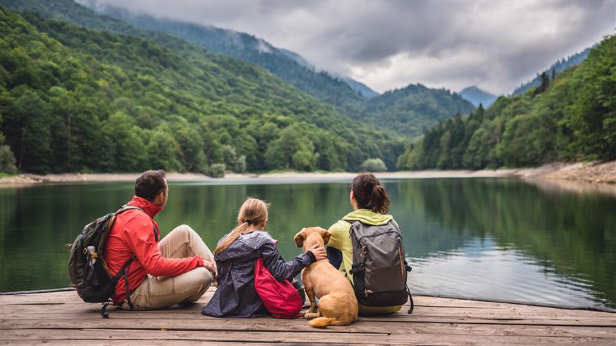 A family, on an outdoor adventure trip, sitting on a dock gazing at a mountain lake. 