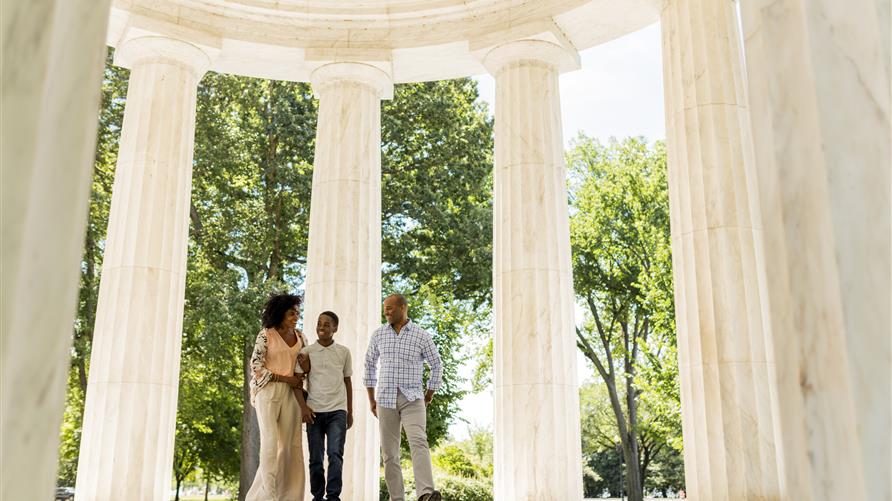 A family of three on vacation in Washington, D.C., posing in front of marble columns. 