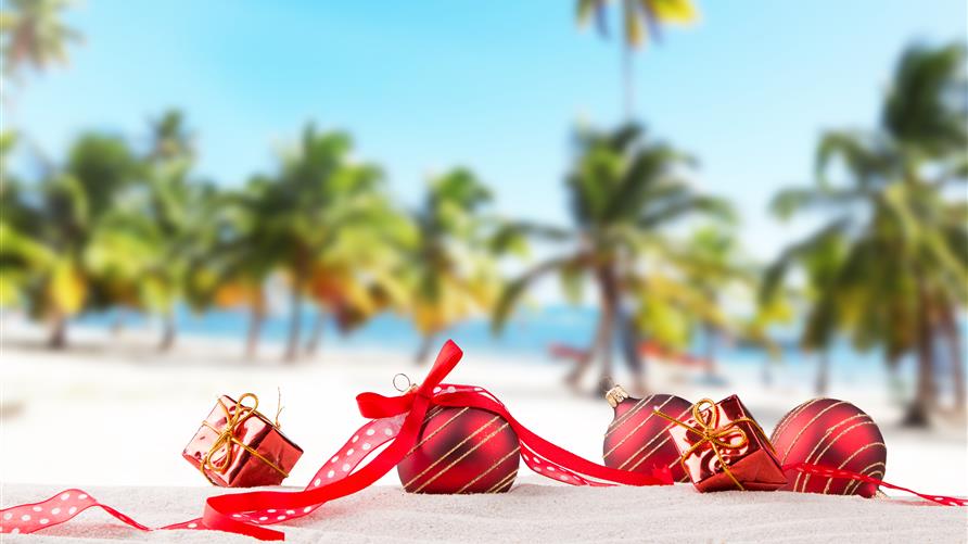 Christmas ornaments laying on the beach with palm trees in the background.