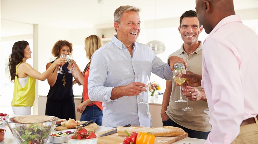 A group of mature friends gathered in their Hilton Grand Vacations resort kitchen socializing and smiling.