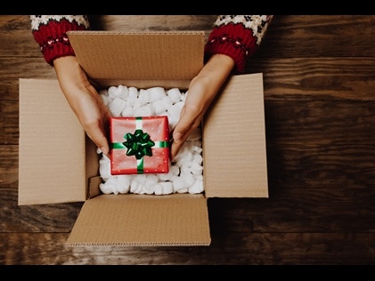 Woman placing a wrapped Christmas gift in a shipping box.