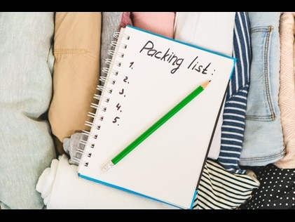A notebook with "packing list" handwritten at the top, laid atop of clothing. 