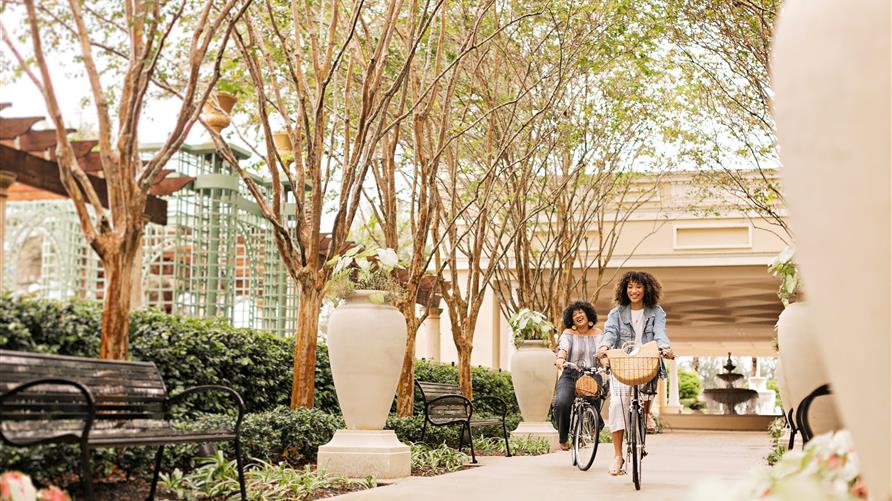 Two women staying at a Hilton Grand Vacations Orlando resort smiling on carefree bike ride on property. 