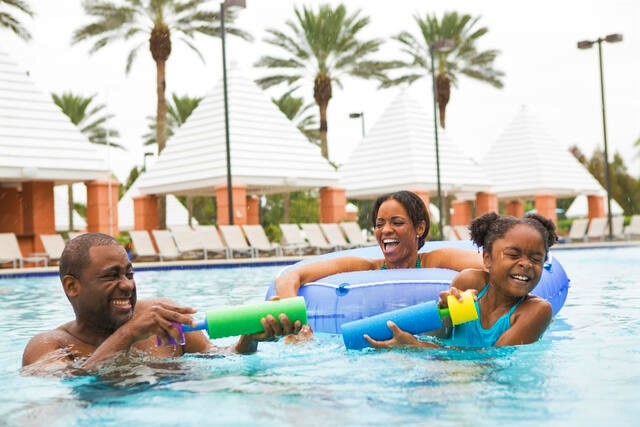 Family playing in the pool with floats and water sprayers at Hilton Grand Vacations at SeaWorld in Orlando, Florida. 
