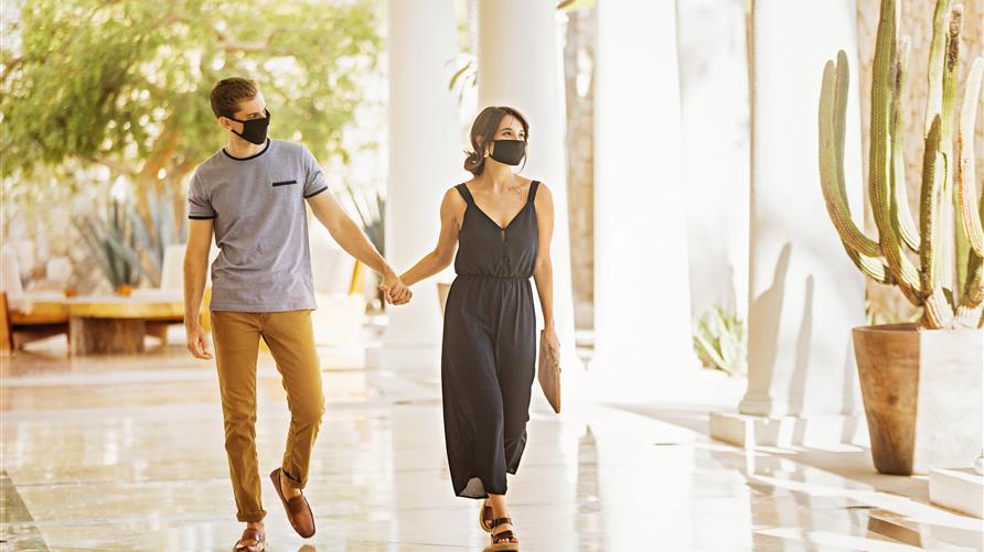 Couple wearing face coverings and holding hands while walking through a breezeway at Los Cabos by Hilton Club in Los Cabos, Mexico. 