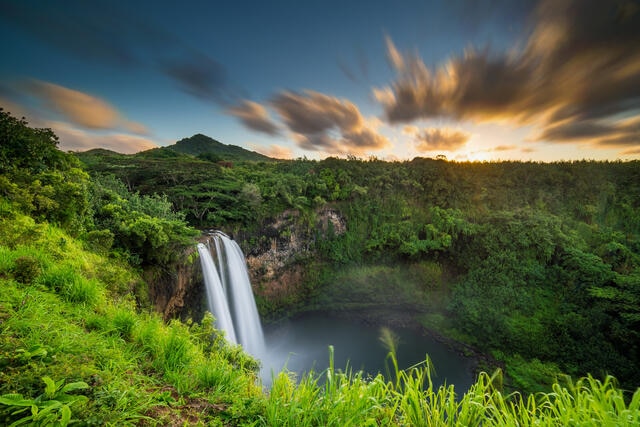 Breathtaking waterfall with blue and orange painted skies above in Maui, Hawaii. 