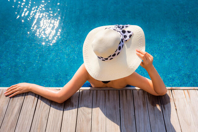 Overhead shot of woman in a wide brimmed floppy hat lounging in a swimming pool.