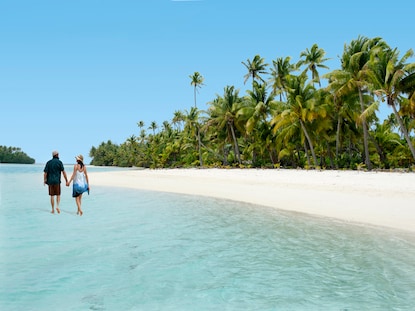 Couple walking hand in hand down the shore on One Foot Island Aitutaki, Cook Islands.