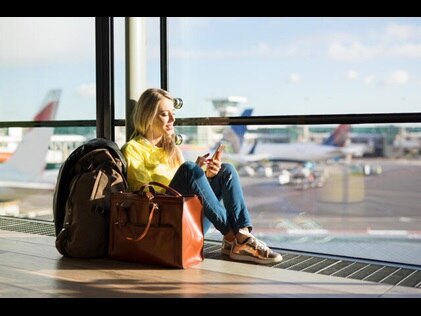 Woman on her phone sitting next to carry on luggage at the airport. 