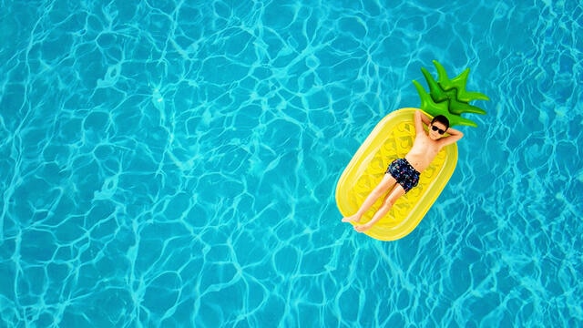Aerial view of young boy lounging on a floating raft in a crystal clear swimming pool at a Hilton Grand Vacations resort. 