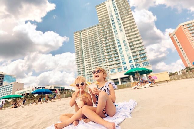 Two young girls enjoying frozen drinks on the beach outside a Hilton Grand Vacations Myrtle Beach resort. 