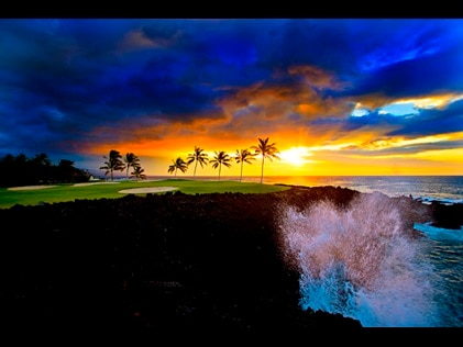 Waves crashing against palm tree line cliff at sunset a Ocean Tower by Hilton Grand Vacations Big Island resort in Hawaii. 