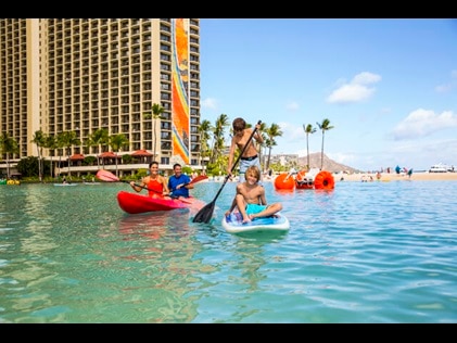 Family paddle boarding in the Hilton Hawaiian Village lagoon while on vacation in Hawaii. 