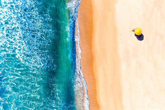 Aerial view of a yellow beach umbrella on the shoreline. 