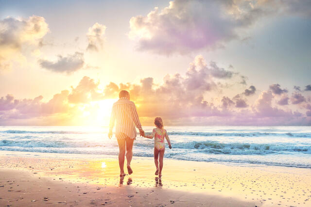 Mother and daughter on beach admiring the sunset. 