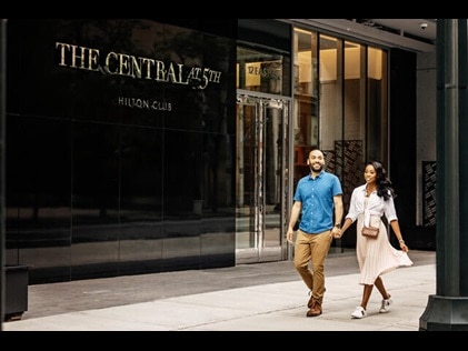 Couple walking hand in hand outside The Central at 5th by Hilton Club in Midtown Manhattan, New York City. 
