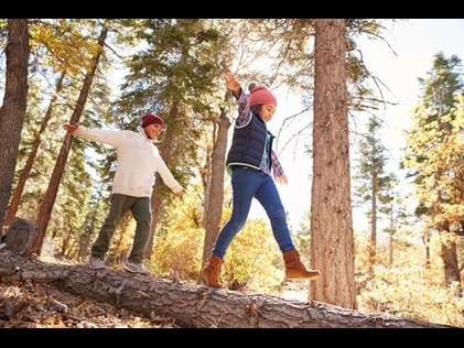 Kids playing on a log surrounded by fall foliage.