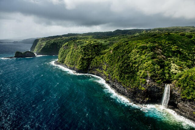 Aerial view of Maui coastline and waterfall spilling into the Pacific Ocean in Hawaii. 
