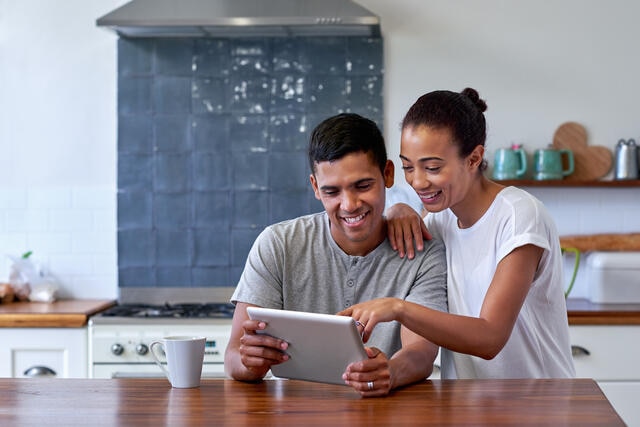 Couple smiling and looking at iPad together in a kitchen. 