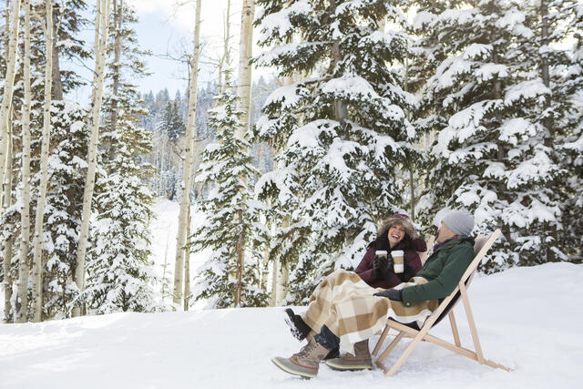 Couple happily enjoying an aprés ski beverage outside in the snow. 