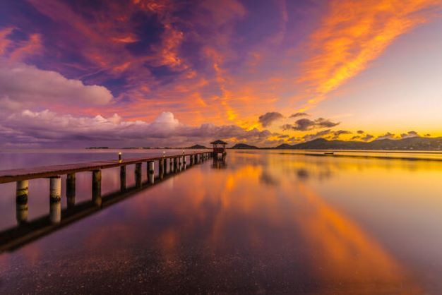 Serene shot of a dock and calm waters with cotton candy sunset skies overhead. 