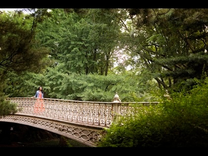 Woman walking across Central Park bridge surrounded by lush greenery, New York, New York. 