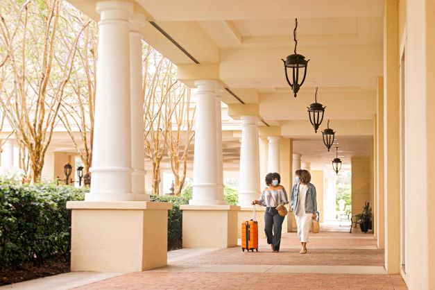 Two woman walking happily into Parc Soleil® by Hilton Grand Vacations with luggage, Orlando, Florida. 
