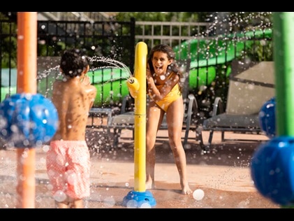 Two kids laughing and playing at a splash pad.