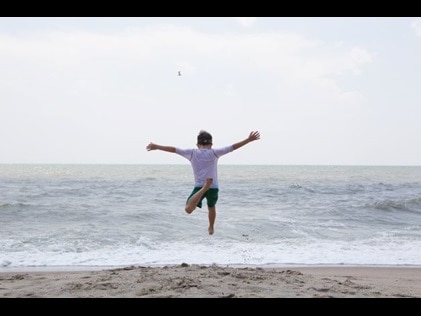 Young boy running and jumping into the ocean at beach, Virginia.