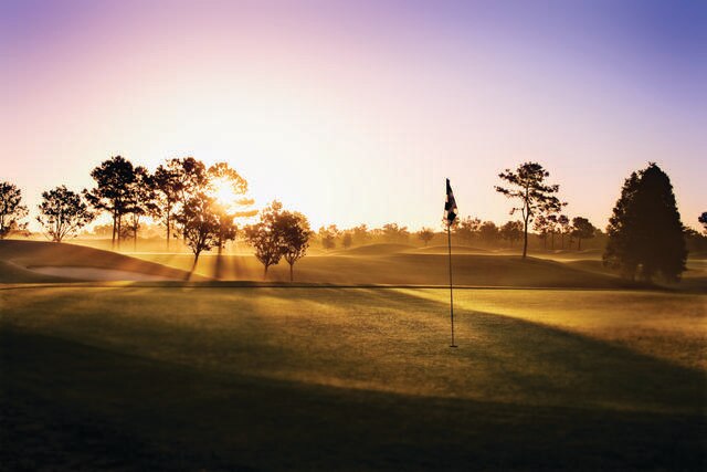 Sunrise lighting the sky over a morning-dew covered golf course. 