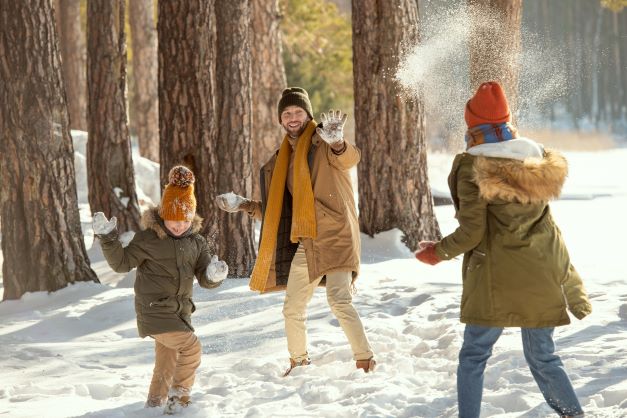 Young family of three throwing hurling snowballs while laughing. 