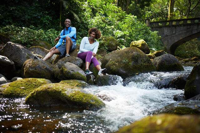Couple enjoying a break from hiking along a stream in a lush Hawaii rainforest, Big Island. 