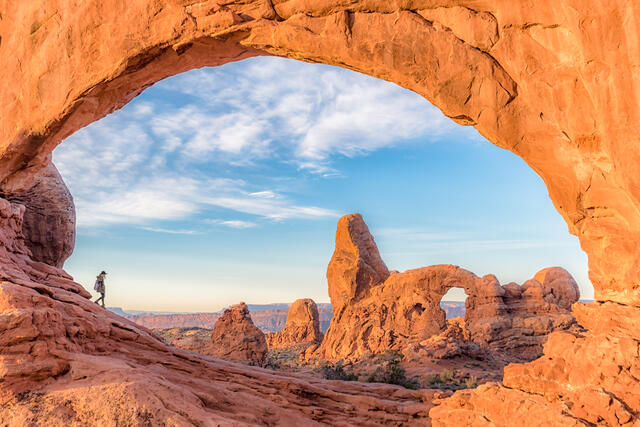 Striking image of hiker walking along the inside of natural red arches, Utah. 
