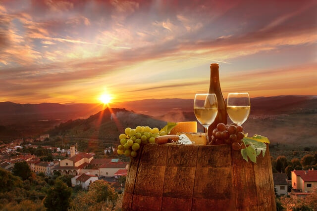 Stunning image of wine, fruit and cheese presentation with rolling hills and sunset in the distance, Tuscany, Italy. 