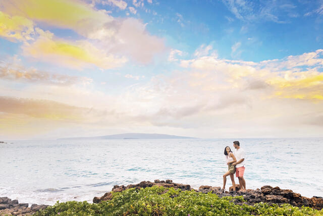 Couple embracing on cliff overlooking ocean, sunset painted skies overhead, Maui, Hawaii. 