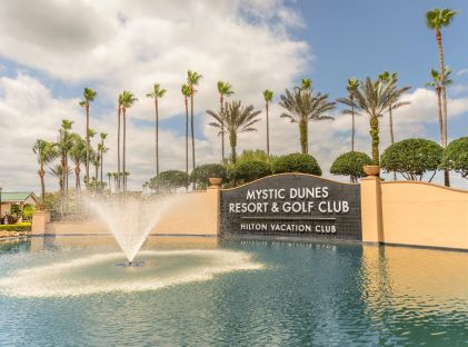 Sign with fountains and palm trees that reads "Mystic Dunes Resort & Golf Club, a Hilton Vacation Club"