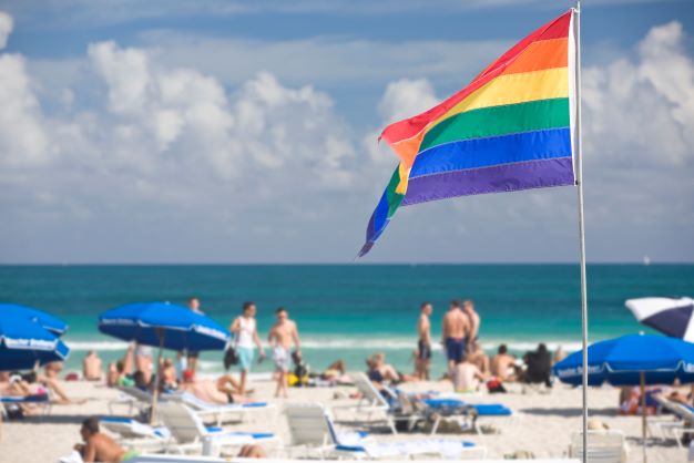 Pride flag on Miami Beach, beachgoers in the distance. 