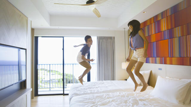 Young boy and girl excitedly jumping on beds while on vacation with Hilton Grand Vacation.