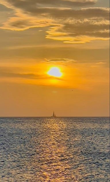 Beautiful image of sail boat on horizon and sinking sun overhead, Aruba. 