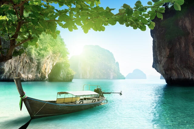 Idyllic tropical scene, including small boat in an emerald-colored lagoon and palm trees, Thailand.