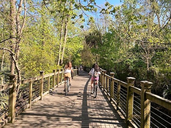 Two young girls riding along wooden, tree-lined bike trail, Hilton Head Island, South Carolina.