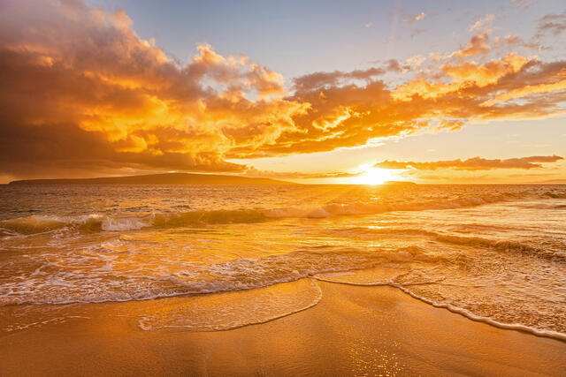 Orange sunrise glow lighting ocean sky, suf washing ashore, Maui, Hawaii. 