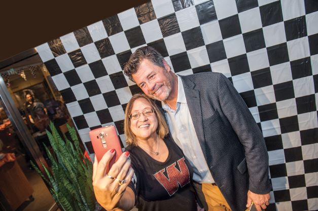 Michael Waltrip taking a selfie with a fan in front of a black-and-white checkered background as part of an exclusive event