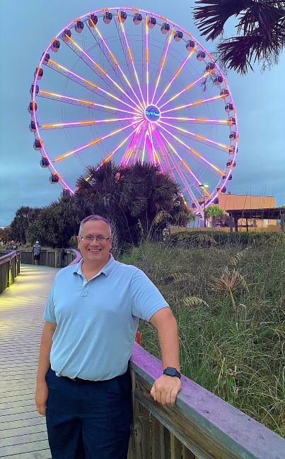 Hilton Grand Vacations Owner posing on boardwalk, SkyWheel lit up in the distance, Myrtle Beach\, South Carolina. 