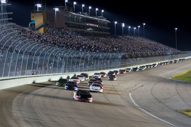 Stock race cars driving on a well-illuminated track at night, a crowd of people watching in the audience, one of the many HGV Ultimate Access experiences Members and Guests can attend