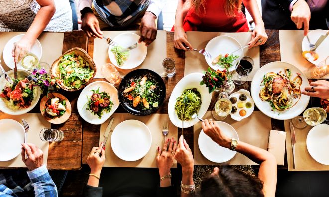 An image taken above a dinner table, as people enjoy a meal from shared plates with salad, pasta, and vegetables