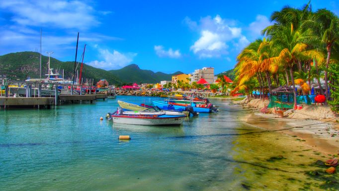 Idyllic Caribbean scene, boats tied along the shoreline, colorful buildings and palm tree-lined beach, Sint Maarten, Caribbean.