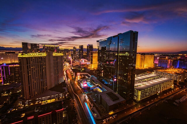 Aerial image of Elara, a Hilton Grand Vacations Club, glowing in the night sky, Strip buzzing with life below, Las Vegas.