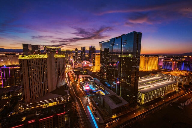 Aerial image of Elara, a Hilton Grand Vacations Club, glowing in the night sky, Strip buzzing with life below, Las Vegas.